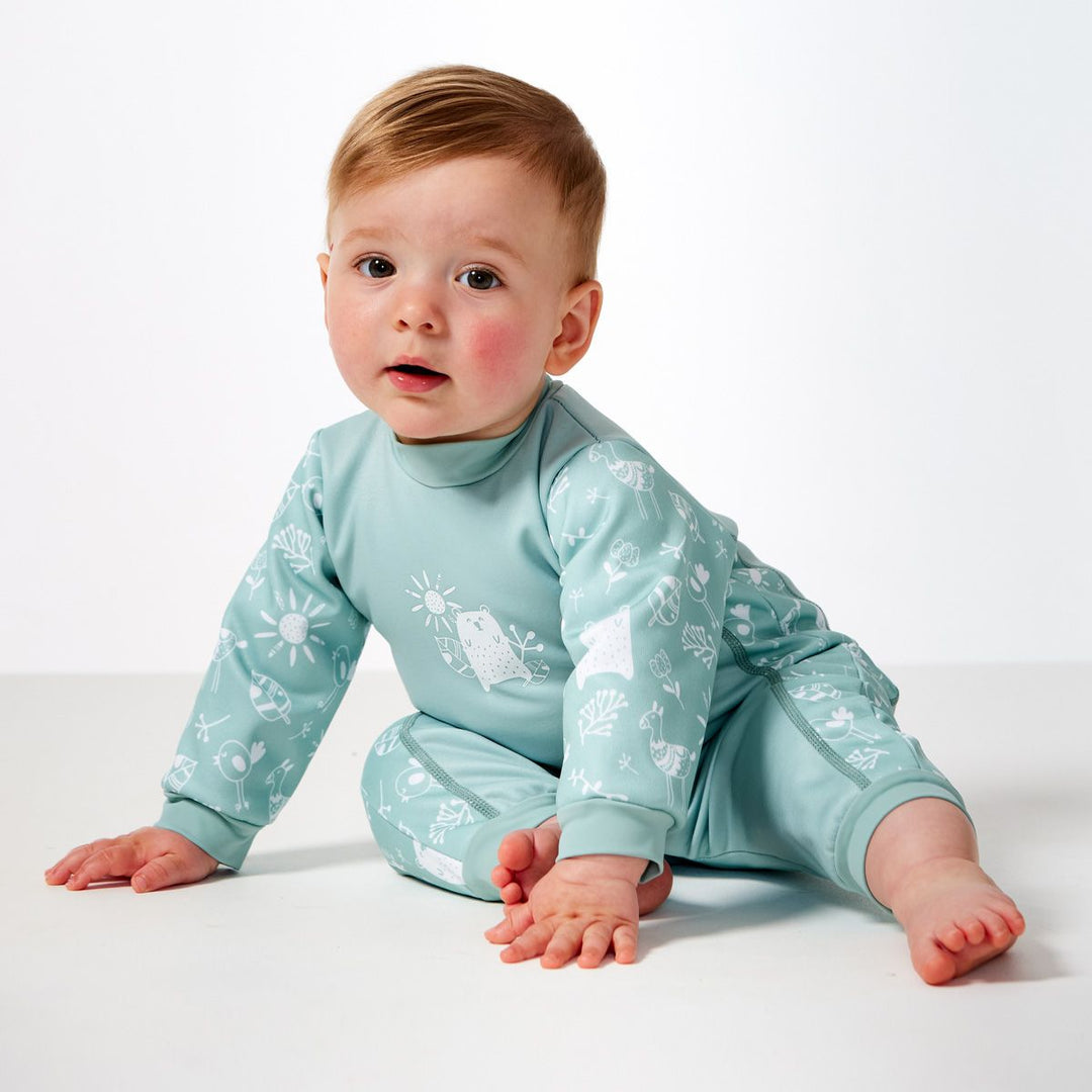 Little one wearing fleece-lined baby wetsuit in greenish blue and white with animals themed print, including bears, llamas, suns and flowers on arms, side panels and chest. Side.