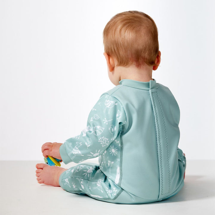 Little one wearing fleece-lined baby wetsuit in greenish blue and white with animals themed print, including bears, llamas, suns and flowers on arms, side panels and chest. Back.