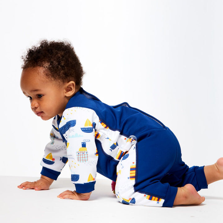 Little one wearing fleece-lined baby wetsuit in navy and white with boats themed print on arms, side panels and chest. Side.