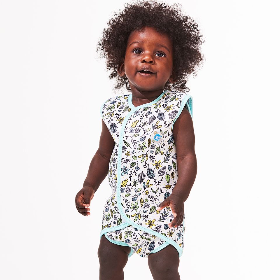 Lifestyle image of toddler wearing a Baby Wrap wetsuit in white with light blue trims and minimalist leaves themed print. 