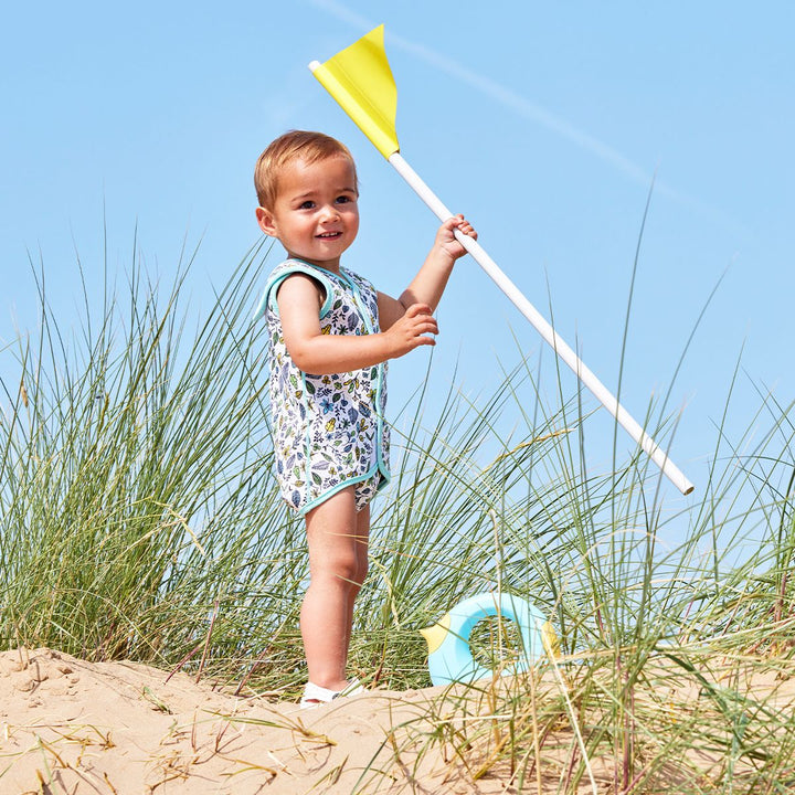 Lifestyle image of toddler wearing a Baby Wrap wetsuit in white with light blue trims and minimalist leaves themed print. 