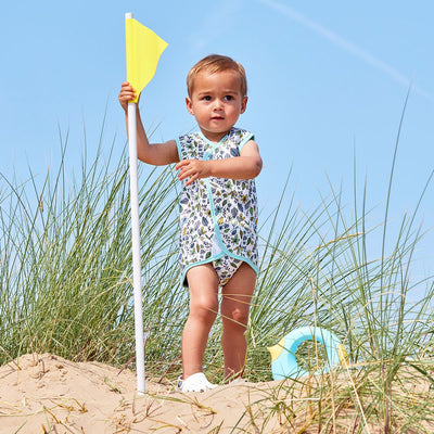 Lifestyle image of toddler wearing a Baby Wrap wetsuit in white with light blue trims and minimalist leaves themed print. 