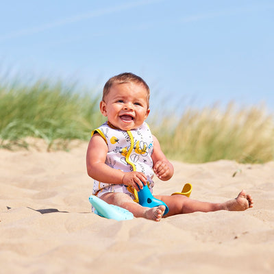 Lifestyle image of baby wearing a Baby Wrap wetsuit in white with yellow trims and minimalist floral themed print. 