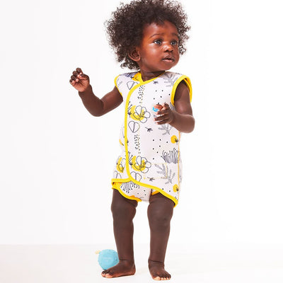 Lifestyle image of toddler wearing a Baby Wrap wetsuit in white with yellow trims and minimalist floral themed print. 