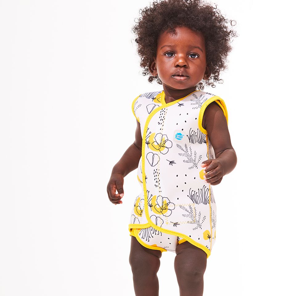 Lifestyle image of toddler wearing a Baby Wrap wetsuit in white with yellow trims and minimalist floral themed print. 