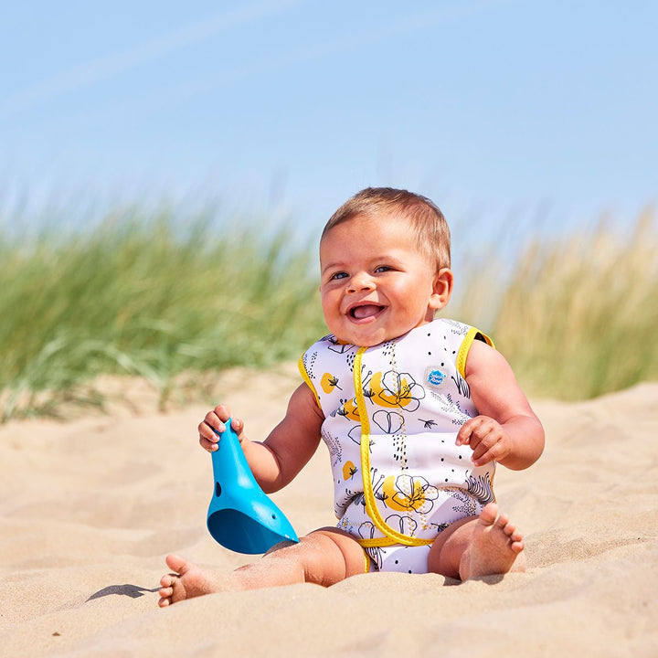 Lifestyle image of baby wearing a Baby Wrap wetsuit in white with yellow trims and minimalist floral themed print. 