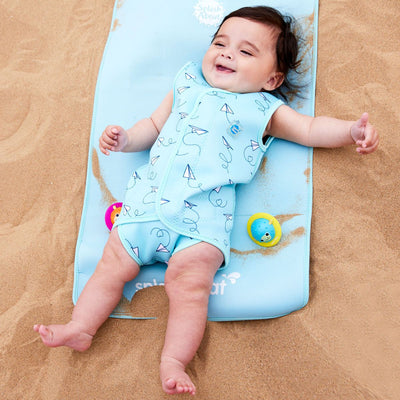 Lifestyle image of baby wearing a Baby Wrap wetsuit in baby blue with white paper planes themed print.