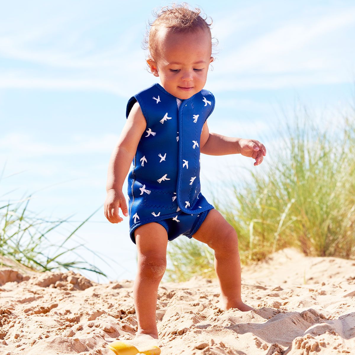 Lifestyle image of toddler wearing a Baby Wrap wetsuit in navy blue with white doves themed print.
