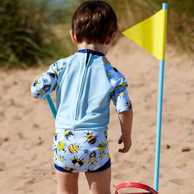 Lifestyle image of toddler wearing Happy Nappy Sunsuit in baby blue with navy blue trims and insects themed print. Back.
