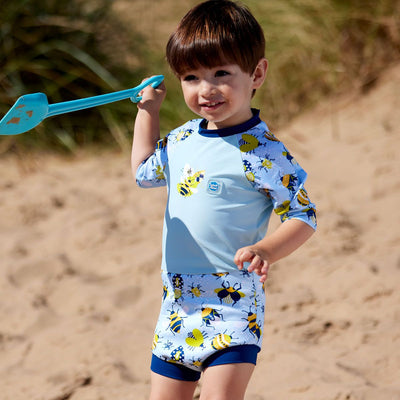 Lifestyle image of toddler wearing Happy Nappy Sunsuit in baby blue with navy blue trims and insects themed print. Front.
