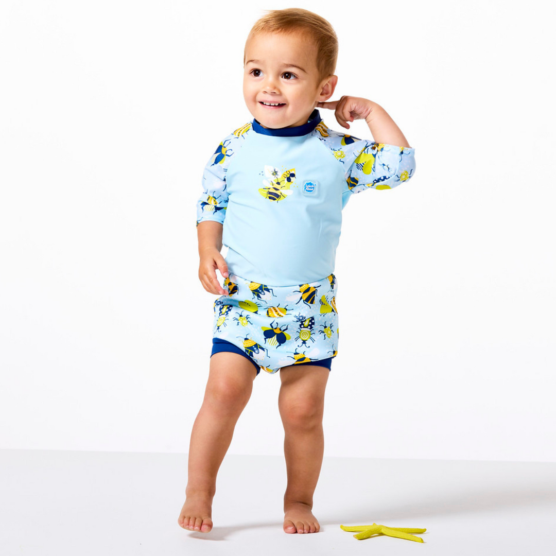 Lifestyle image of toddler wearing Happy Nappy Sunsuit in baby blue with navy blue trims and insects themed print. Front.