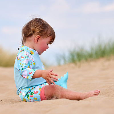 Lifestyle image of toddler wearing a Happy Nappy Sunsuit in light blue and little ducks themed print on sleeves and swim nappy.