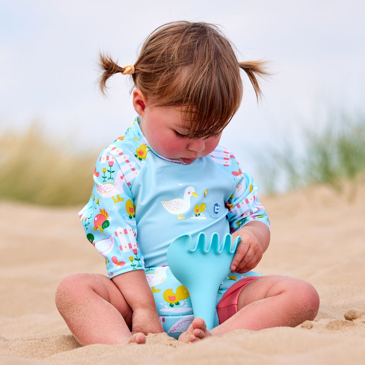 Lifestyle image of toddler wearing a Happy Nappy Sunsuit in light blue and little ducks themed print on sleeves and swim nappy. Back.