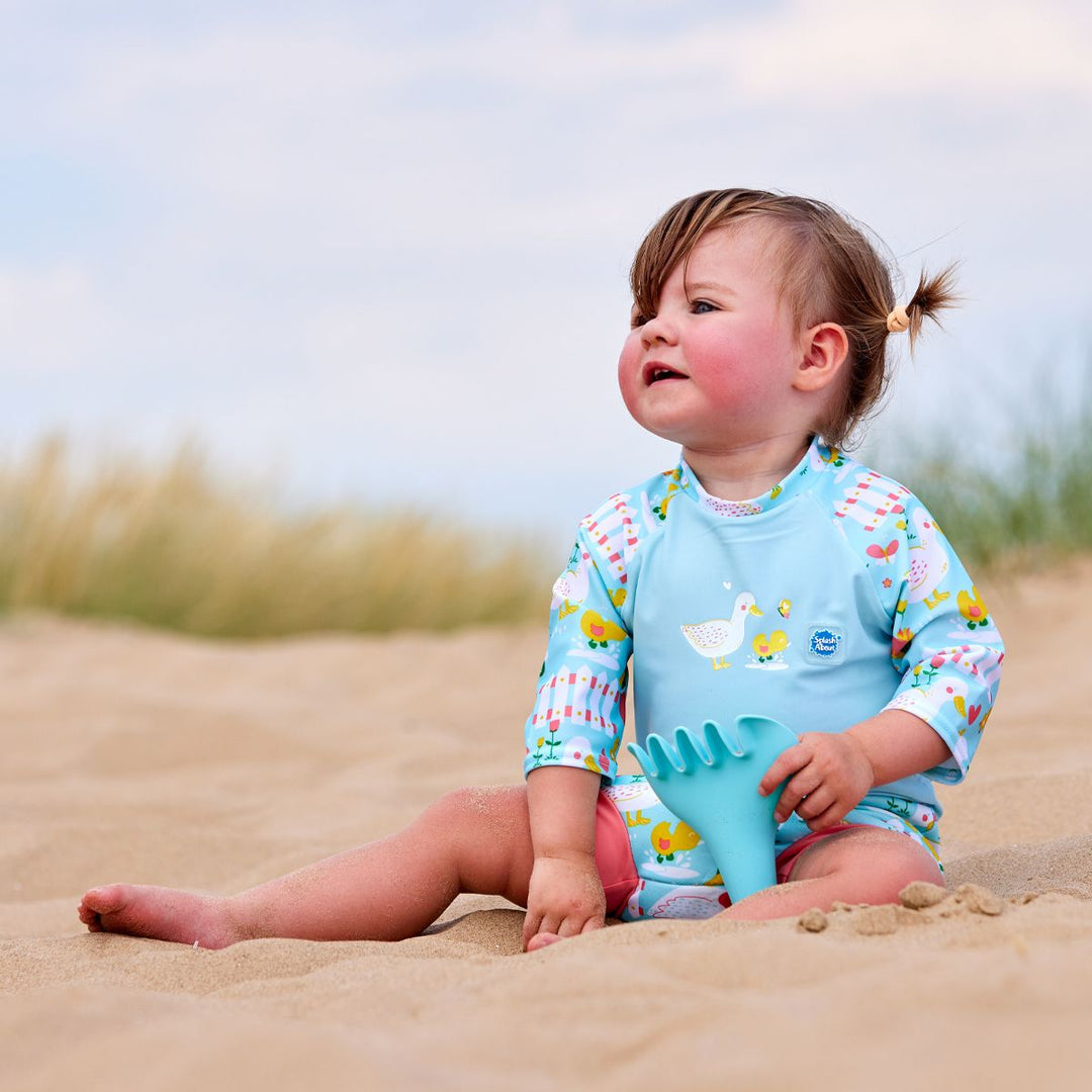 Lifestyle image of toddler wearing a Happy Nappy Sunsuit in light blue and little ducks themed print on sleeves and swim nappy. Front.