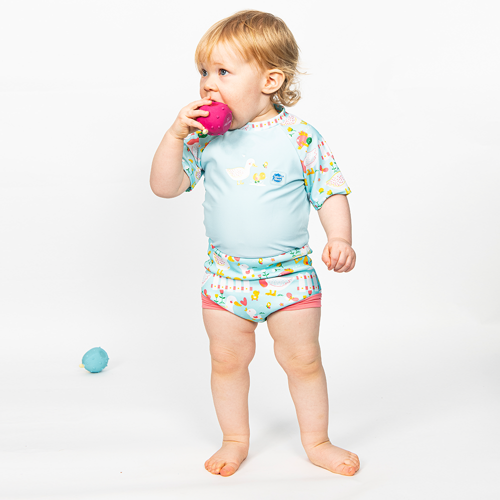 Lifestyle image of toddler wearing a Happy Nappy Sunsuit in light blue and little ducks themed print on sleeves and swim nappy. Front.