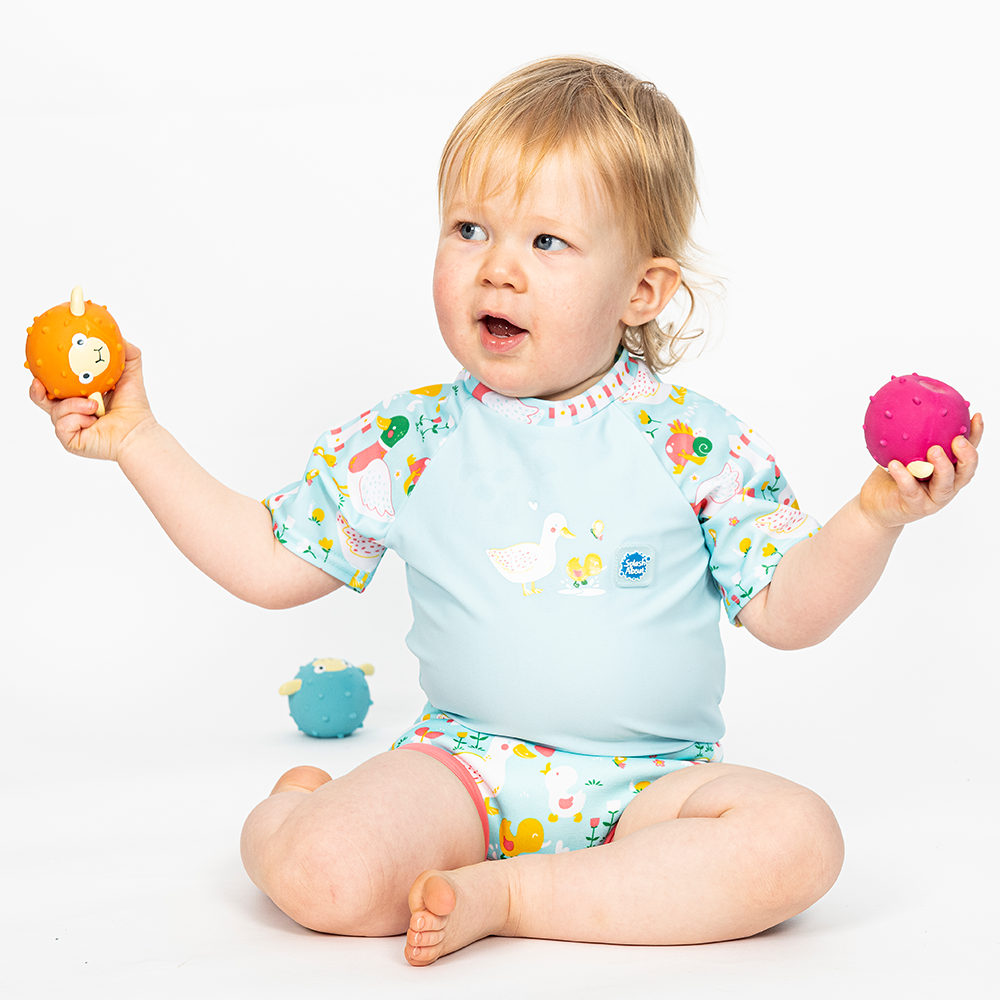 Lifestyle image of toddler wearing a Happy Nappy Sunsuit in light blue and little ducks themed print on sleeves and swim nappy. Front.