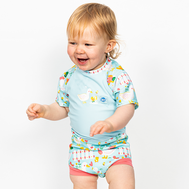 Lifestyle image of toddler wearing a Happy Nappy Sunsuit in light blue and little ducks themed print on sleeves and swim nappy. Front.