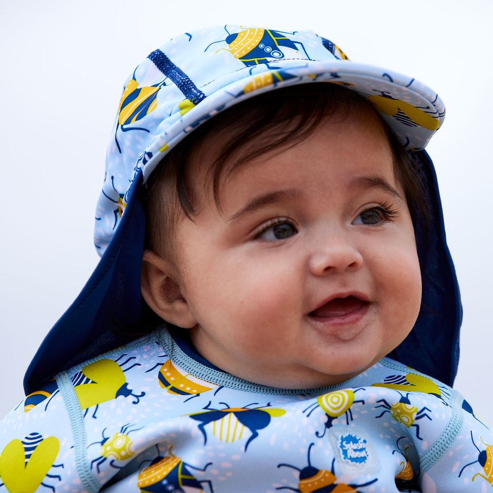 Lifestyle image of toddler wearing a legionnaire style sun hat in the beach. The hat is light blue and navy blue, with insects themed print panel. He's also wearing matching Happy Nappy wetsuit. Close-up.