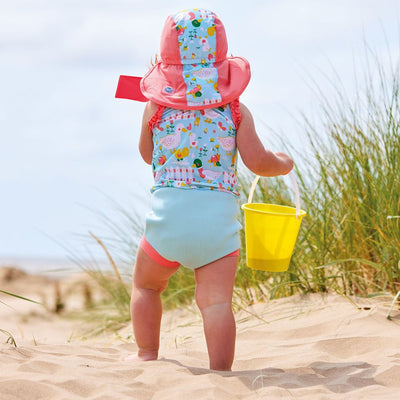 Lifestyle image of toddler wearing a legionnaire style sun hat in the beach. The hat is reddish pink and light blue, with little ducks themed print panel including ducks, snails, flowers and more. She's also wearing matching Happy Nappy costume. Back.