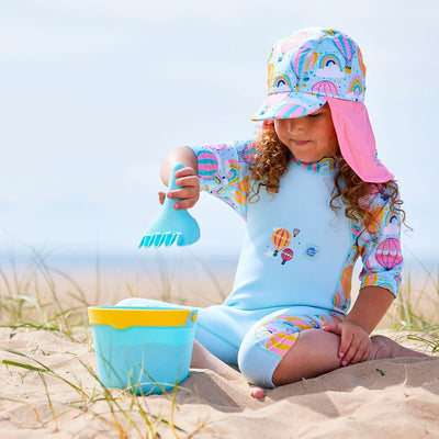 Lifestyle image of child wearing a legionnaire style sun hat in baby blue and pink, with hot air balloons themed print panel, including clouds and rainbows. She's also wearing a matching Sun & Sea Wetsuit.