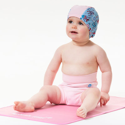 Toddler wearing  swim hat in light blue with baby pink trims and under the sea themed print, including treasure chests, fish, jellyfish, starfish, seahorse and more. She's also wearing an Almond Blossom Happy Nappy.