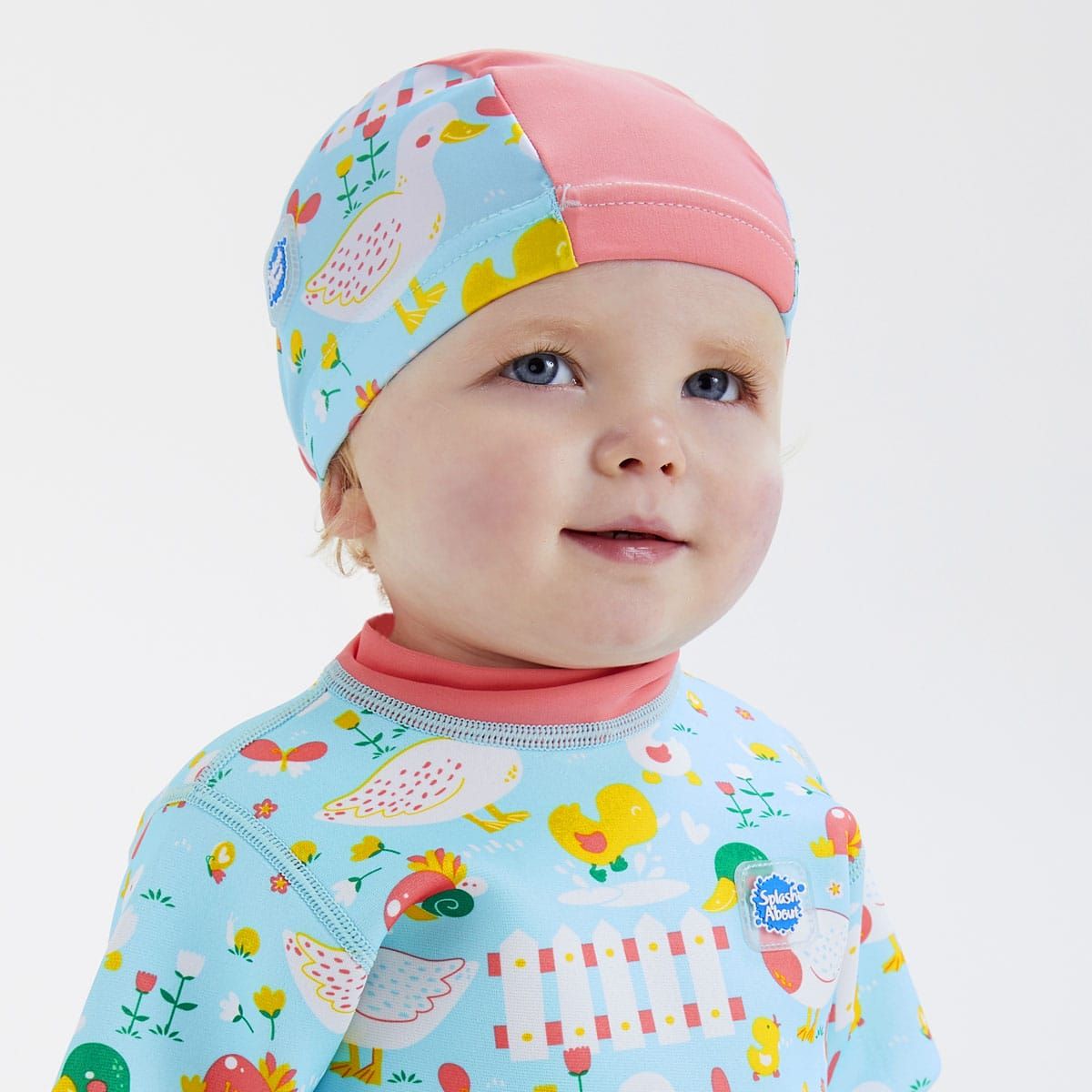 Toddler wearing  swim hat in light blue with pink trims and little ducks themed print.