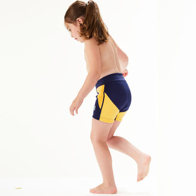 Lifestyle image of child wearing neoprene swim shorts in navy blue with yellow trims. Back.