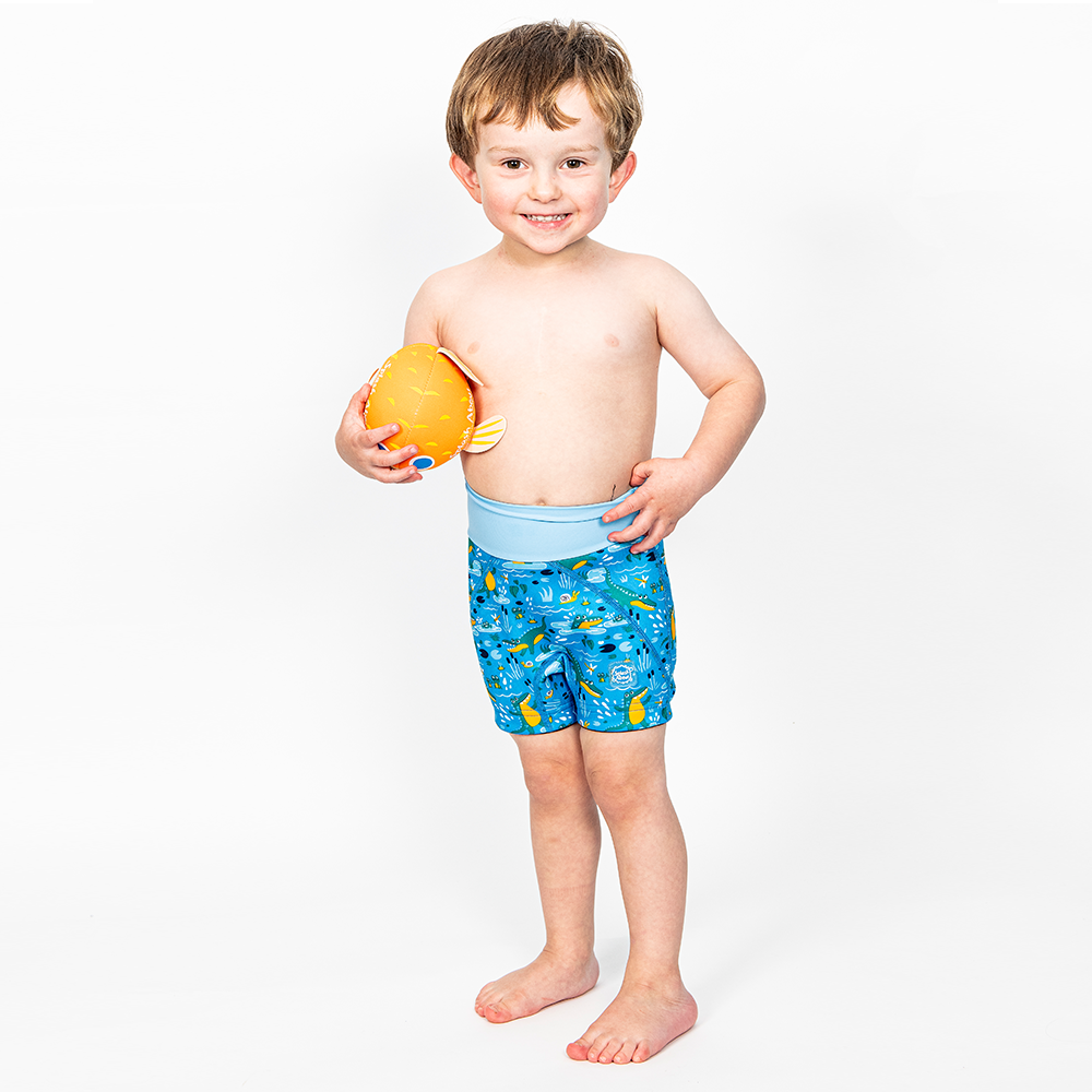 Lifestyle image of toddler wearing neoprene swim shorts in blue with light blue waist and swamp themed print, including crocodiles, frogs, snails and more.