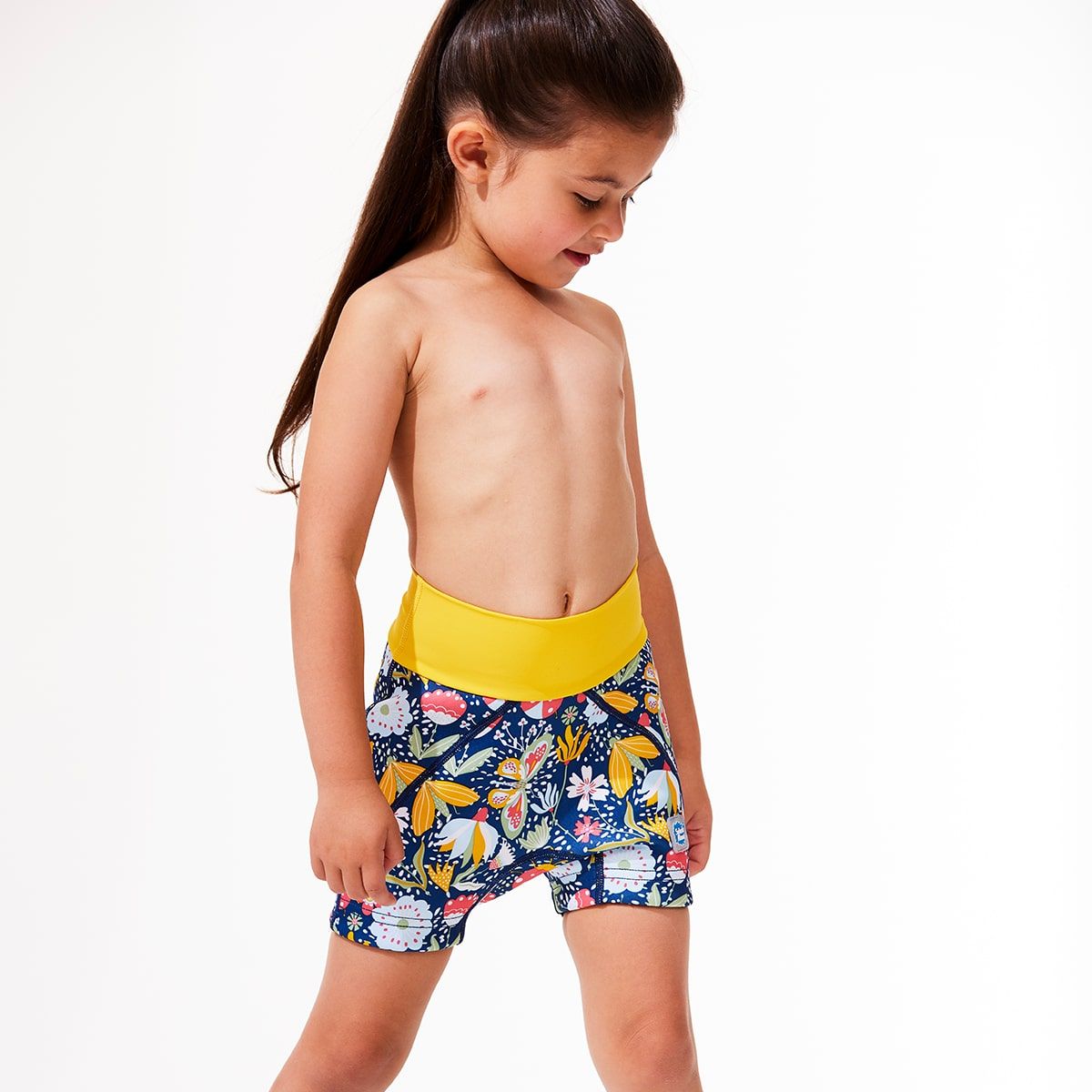 Lifestyle image of toddler wearing neoprene swim shorts in navy blue with yellow waist and floral print.