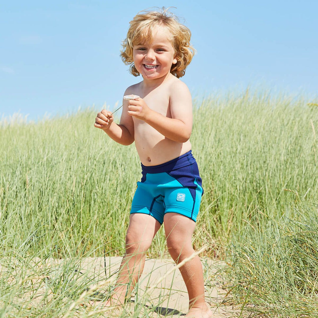 Lifestyle image of child wearing neoprene swim shorts in navy blue and jade.