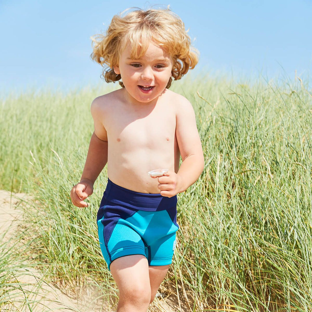 Lifestyle image of child wearing neoprene swim shorts in navy blue and jade.