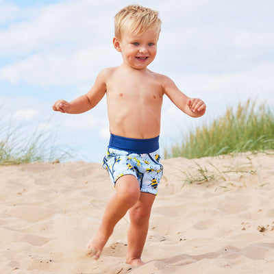 Lifestyle image of toddler wearing neoprene swim shorts in light blue with navy blue trims and insects print. 