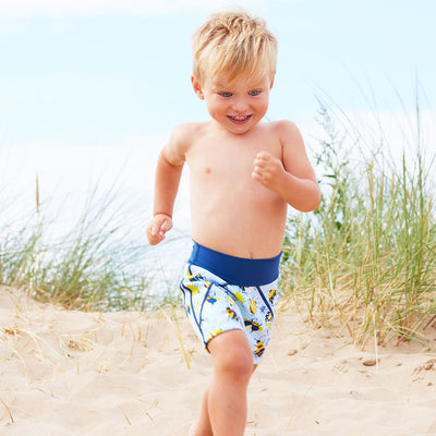Lifestyle image of toddler wearing neoprene swim shorts in light blue with navy blue trims and insects print. 