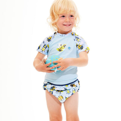 Lifestyle image of toddler wearing UV protective short sleeve rash top in light blue, and insects themed print on the chest and sleeves. He's also wearing matching under nappy.