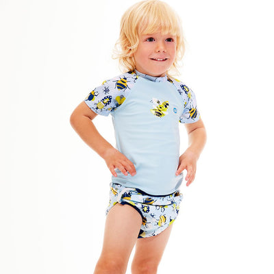 Lifestyle image of toddler wearing UV protective short sleeve rash top in navy blue, and insects themed print on the chest and sleeves. He's also wearing matching adjustable under nappy.