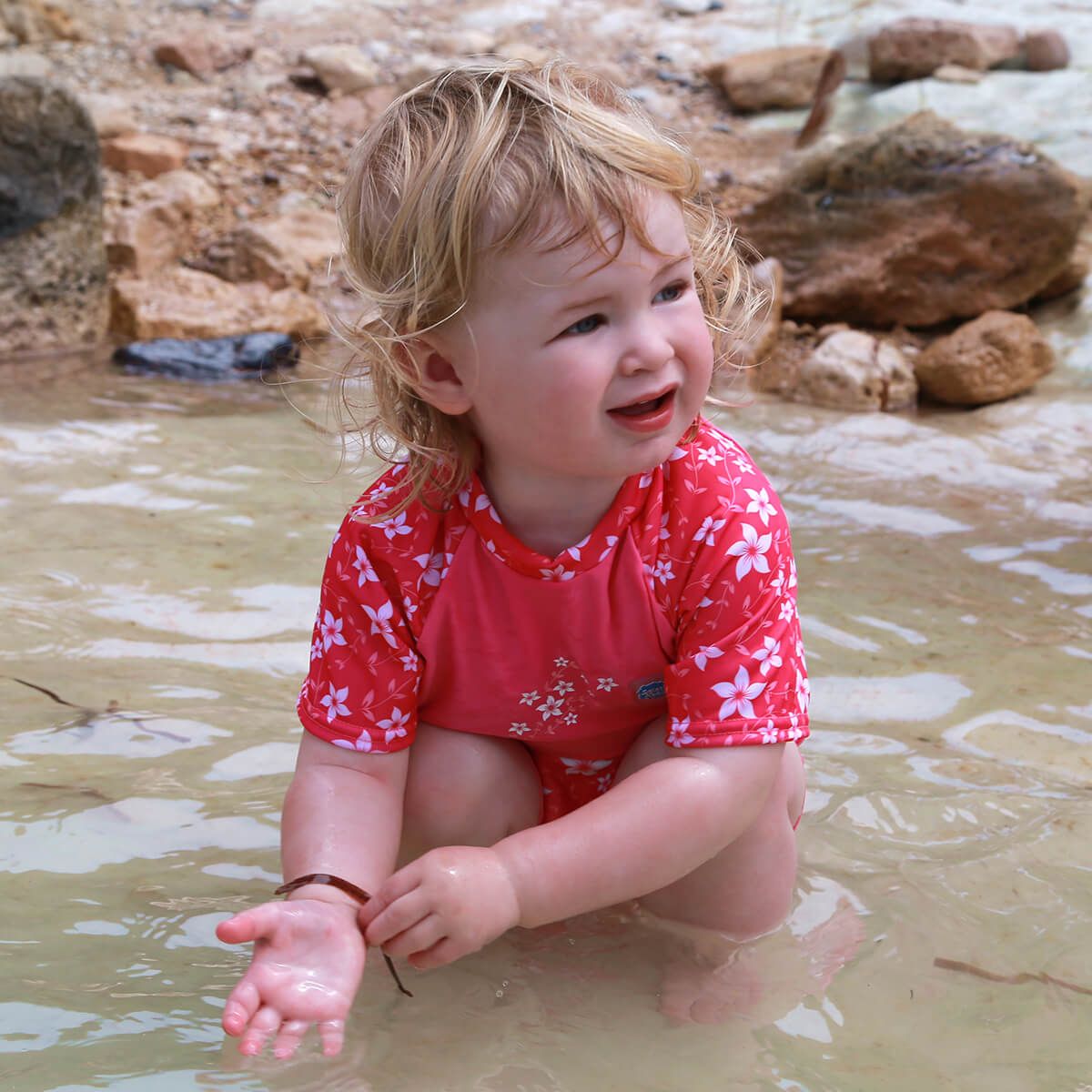 Lifestyle image of toddler wearing UV protective short sleeve rash top in pink, and floral print on the chest and sleeves. They're also wearing matching jammers.