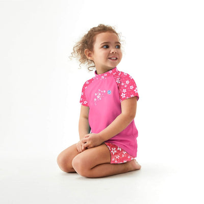 Lifestyle image of toddler wearing UV protective short sleeve rash top in pink, and floral print on the chest and sleeves. She's also wearing matching jammers.