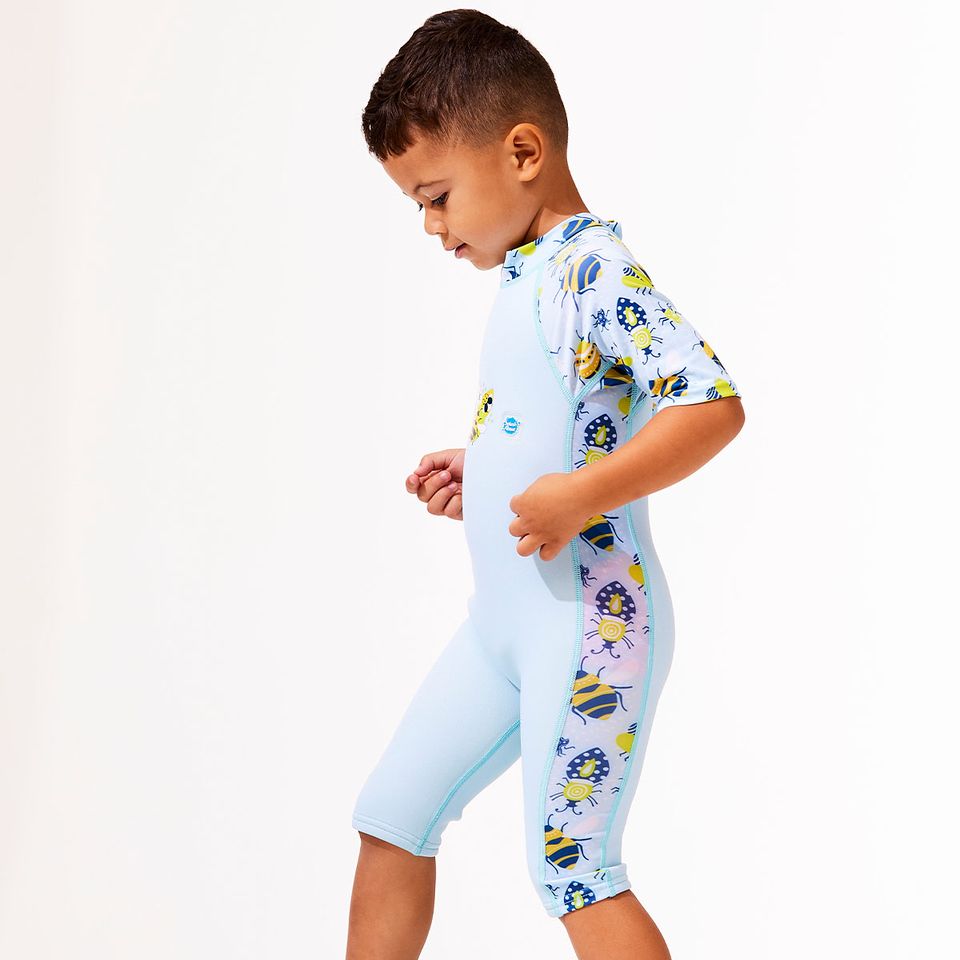 Lifestyle image of child wearing a one piece UV sun and sea wetsuit for toddlers in light blue with navy blue trims. Insects themed print on sleeves, side panels and neck. 