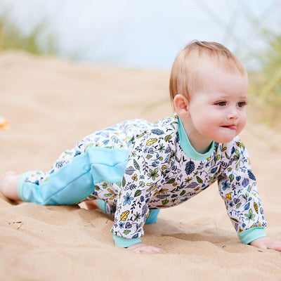 Lifestyle image of baby wearing a fleece-lined baby wetsuit in white with light blue trims and leaves themed print. 