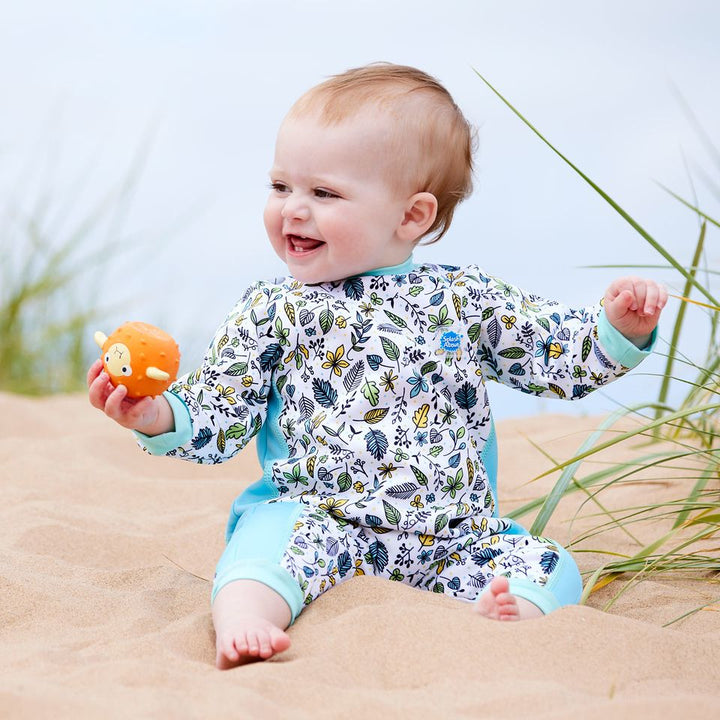 Lifestyle image of baby wearing a fleece-lined baby wetsuit in white with light blue trims and leaves themed print. 