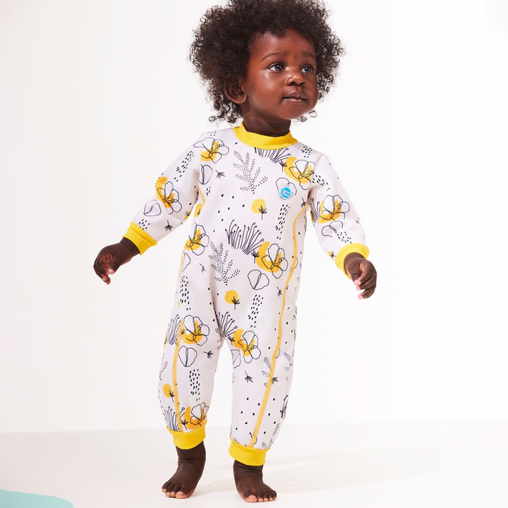 Lifestyle image of baby wearing a fleece-lined baby wetsuit in white with yellow trims and minimalist floral print. 