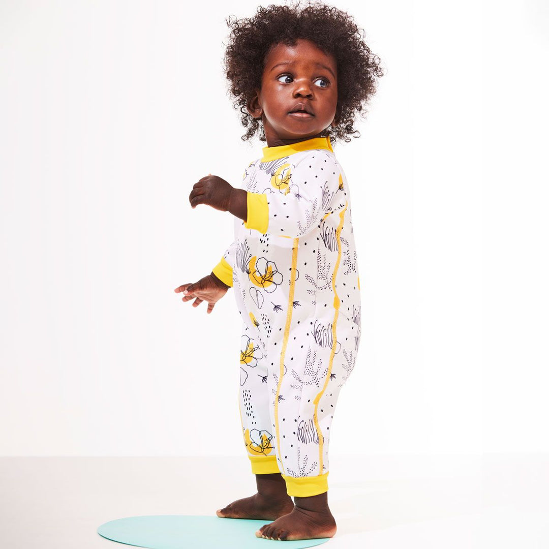 Lifestyle image of baby wearing a fleece-lined baby wetsuit in white with yellow trims and minimalist floral print. 
