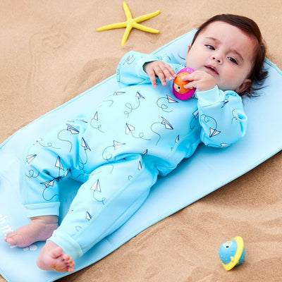 Lifestyle image of baby wearing a fleece-lined baby wetsuit in baby blue and minimalist paper planes print. 