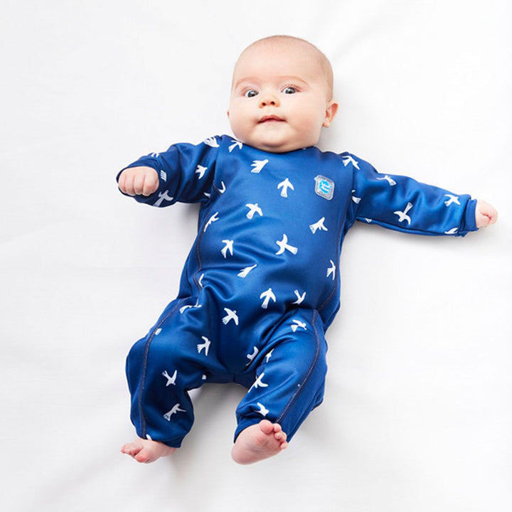 Lifestyle image of baby wearing a fleece-lined baby wetsuit in navy blue and minimalist white doves print. 